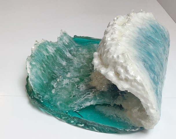 A resin sculpture of a cresting ocean wave. The ocean base is blue-green and the wave rising from it is white.