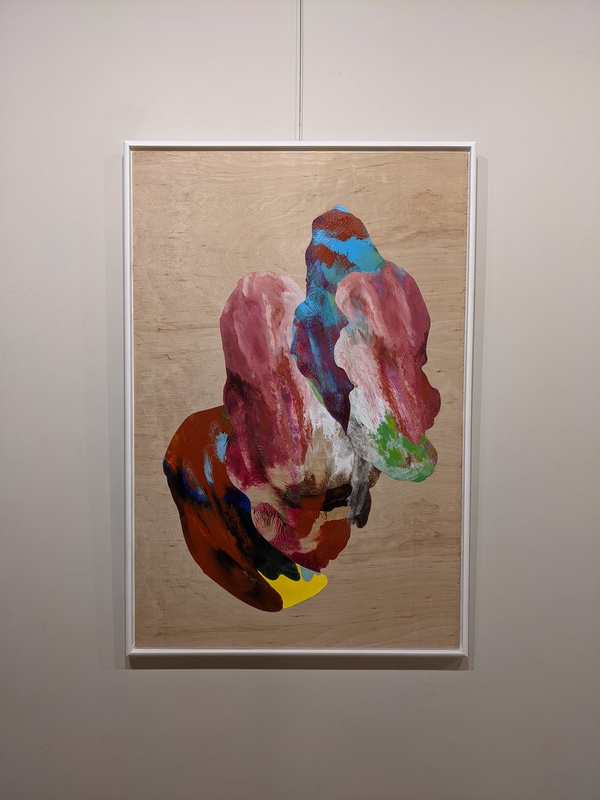 A photograph of an abstract acrylic painting on a wood block. The painting is many colors blurred together, primarily shades of red and pink. The bottom edge is rimmed by brown with a yellow tip, and the very top has veins of blue. 