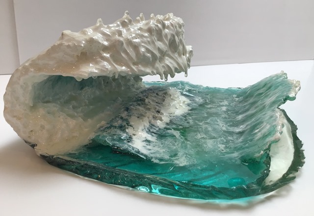 A resin sculpture of a cresting ocean wave. The ocean base is blue-green and the wave rising from it is white.