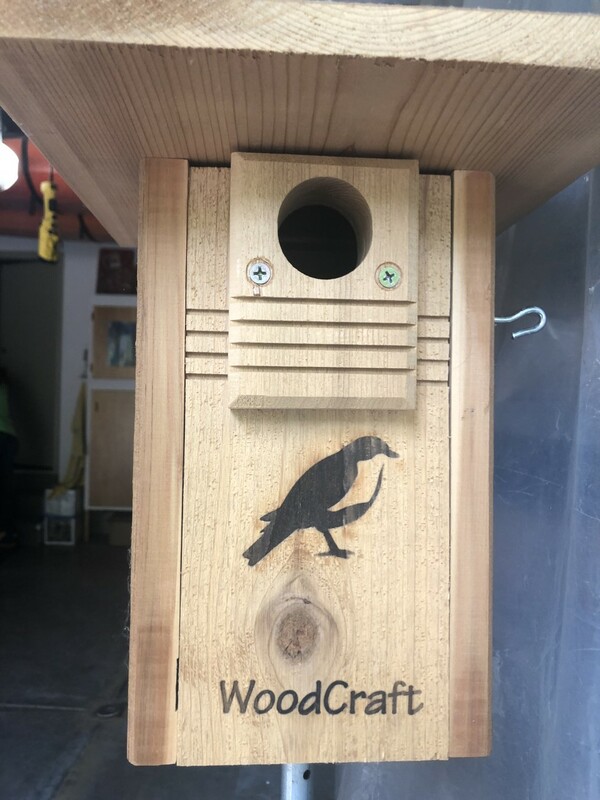 A wooden bird house with an engraving of a bird and the word “WoodCraft” on the front.